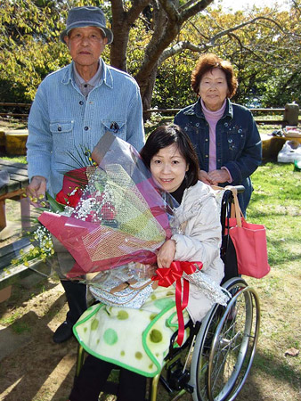花束を持つ車イスの蛭田さんと、後ろにご両親の写真