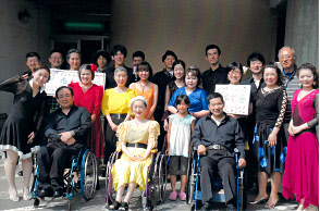 写真：石巻身体障害者歩む会の皆さんの集合写真。車いすを利用している人やボランティアたちが黄色や赤など色とりどりのダンス衣装を身にまとっている。